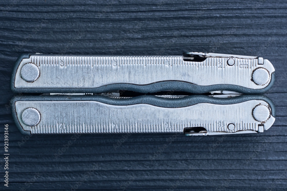 one gray metal closed multitool lies on black wooden table one gray metal closed multitool lies on black wooden table