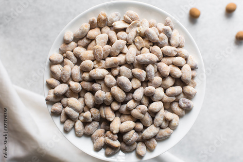 Overhead view of raw coated peanuts on a white plate, flatlay of peanuts coated in egg and flour on a marble countertop, top view of nigerian peanut snack