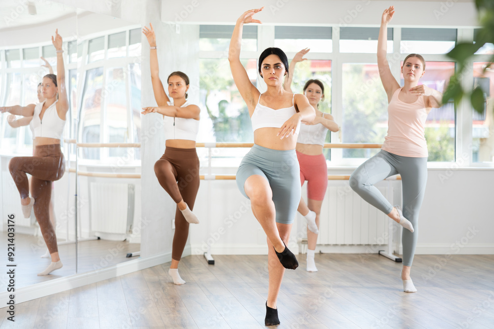 Obraz premium Slender young female attendee of dancing classes training ballet positions together with other group members