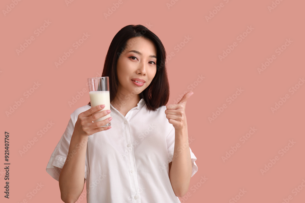 Beautiful Asian woman with glass of milk showing thumb-up on pink background Beautiful Asian woman with glass of milk showing thumb-up on pink background
