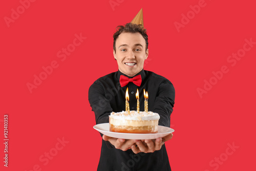 Young man with birthday cake on red background