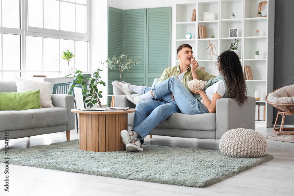 Happy young couple with bowl of popcorn sitting on sofa at home Happy young couple with bowl of popcorn sitting on sofa at home