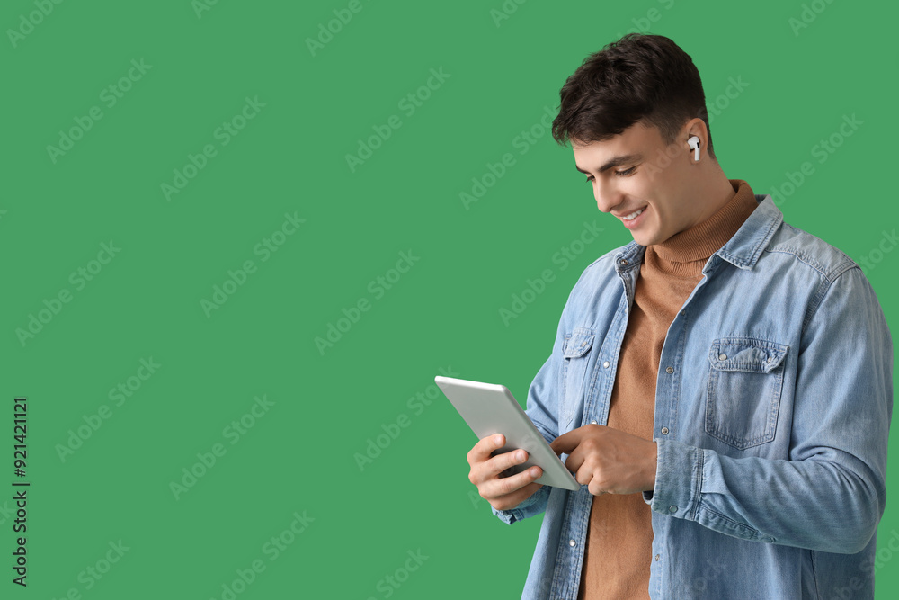 Young man in earphones using tablet computer on green background Young man in earphones using tablet computer on green background