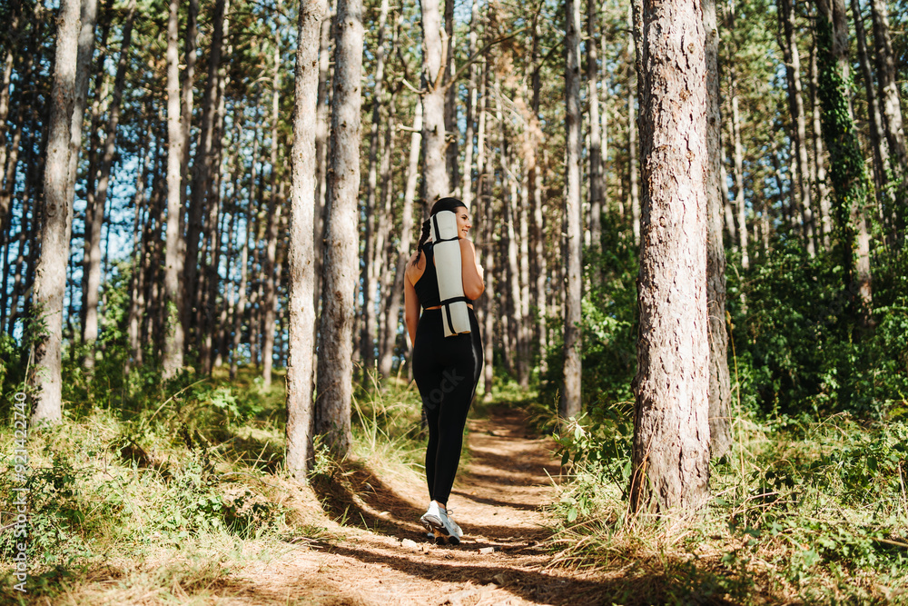 Obraz premium Young caucasian woman walking through forest with yoga mat 