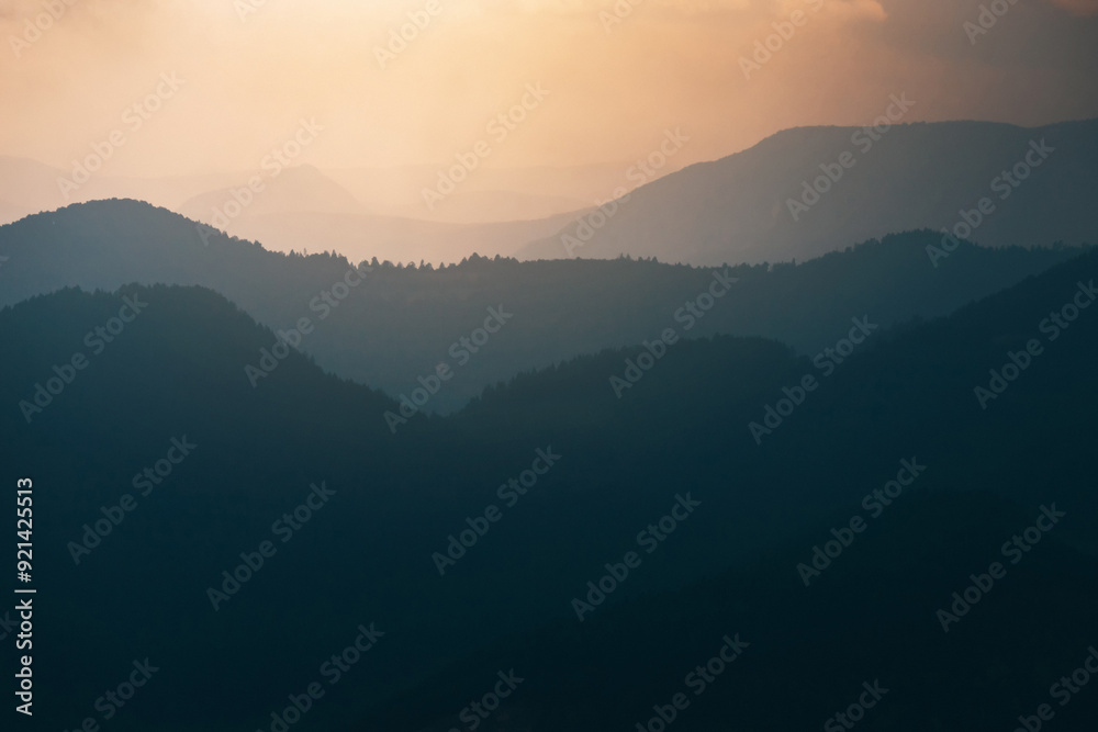 The silhouette of a mountain ridge emerges from the morning fog, with a sunrise pastel sky and the first light of dawn illuminating the landscape