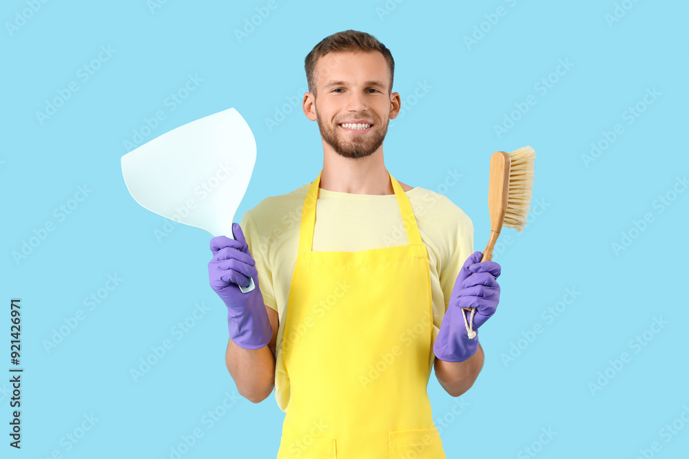 Male janitor in rubber gloves holding dust pan and brush on blue background Male janitor in rubber gloves holding dust pan and brush on blue background