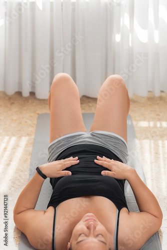 Latin woman in her 40s lying on her back with hands over her stomach, breathing and relaxing at home..