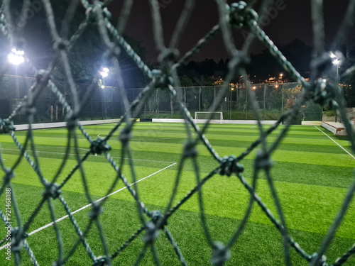 Soccer field or pitch with artificial grass behind the mesh in the sports complex arena in the night.