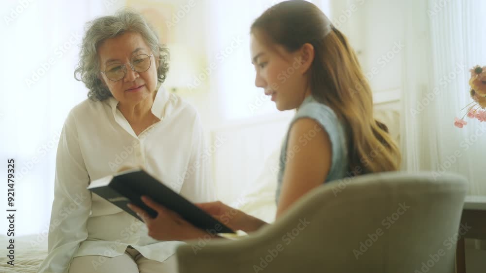 Happy Asian senior mature woman reading a book with caregiver in bedroom. Happy elderly woman enjoy indoor activity lifestyle at home. Senior people mental health care, nursing and caregiving concept. Happy Asian senior mature woman reading a book with caregiver in bedroom. Happy elderly woman enjoy indoor activity lifestyle at home. Senior people mental health care, nursing and caregiving concept.