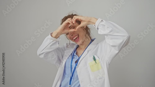 Heartwarming portrait of a happy young caucasian woman in a doctor's coat forming a loving heart symbol with her hands, a sweet gesture of romance against an isolated white background.