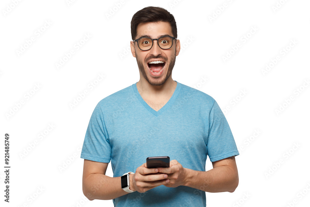 Young handsome manin blue t-shirt, wearing eyeglasses, holding phone in hands, looking at camera with excited WOW face Young handsome manin blue t-shirt, wearing eyeglasses, holding phone in hands, looking at camera with excited WOW face