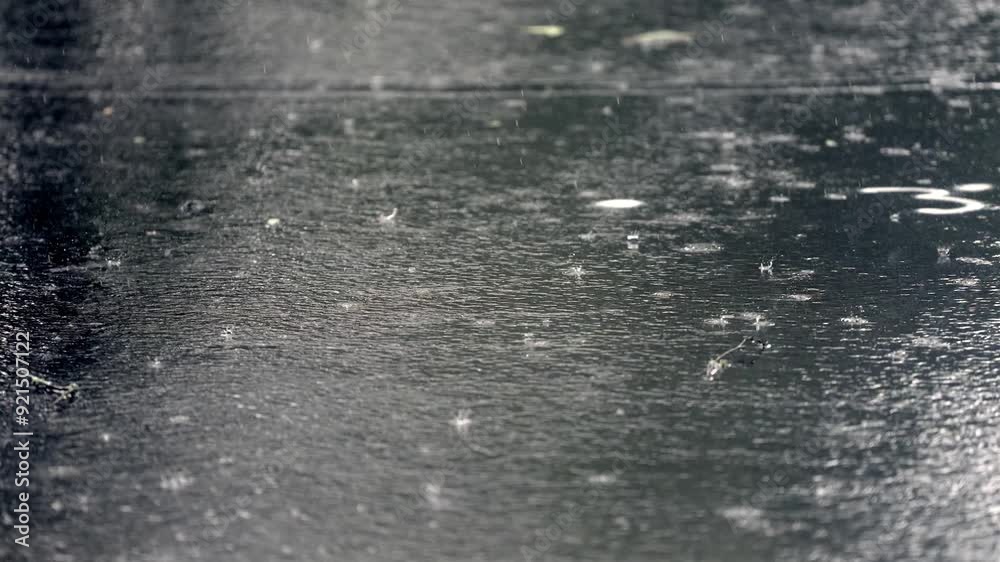 Heavy rain pelting dark asphalt, creating ripples and splashes. Zoomed shot.