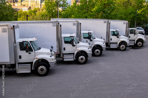 Multiple refrigerator cargo trucks in straight row at parking lot. Transportation, freight, supply chain, logistics, delivery, rising fuel prices concept.