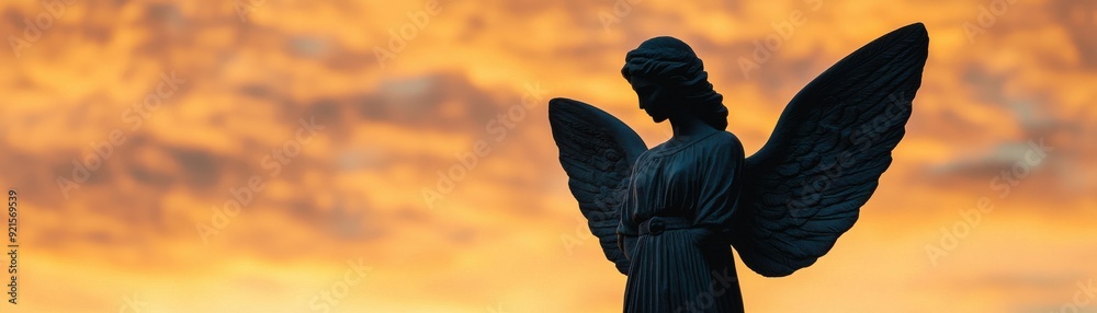 Fototapeta premium A silhouette of an angel statue against a dramatic sunset sky, embodying serenity and spirituality.
