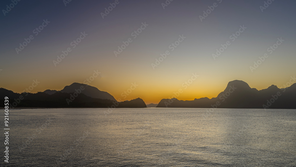 A mysterious evening after sunset. Bizarre silhouettes of mountains against a purple sky, illuminated by orange at the horizon. The ocean is calm. Long exposure. Philippines. Palawan. El Nido. A mysterious evening after sunset. Bizarre silhouettes of mountains against a purple sky, illuminated by orange at the horizon. The ocean is calm. Long exposure. Philippines. Palawan. El Nido.