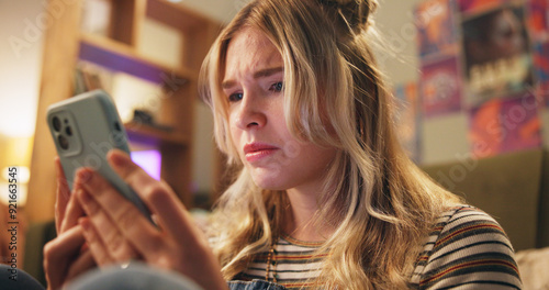 Sad, online and girl with phone in bedroom depressed for bad news, cyber bully and breakup chat. Communication, home and person on smartphone for social media, website and internet for rude text