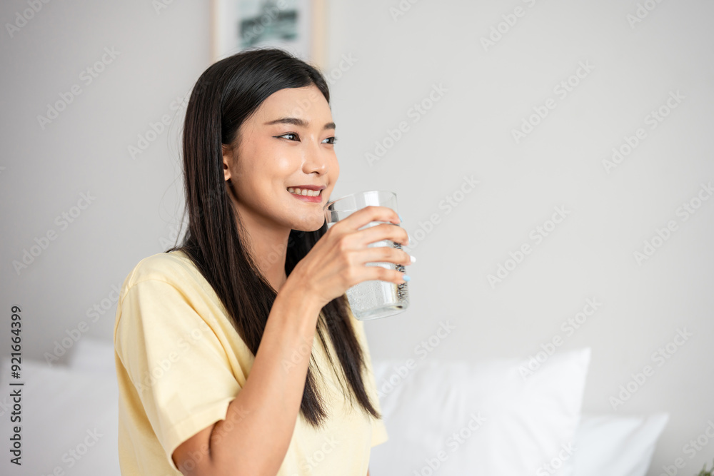 Asian attractive woman sit on bed, drink a glass of water in bedroom. Asian attractive woman sit on bed, drink a glass of water in bedroom.