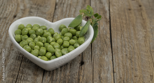 Rustic wooden table adorned with a heart-shaped bowl filled with fresh green peas