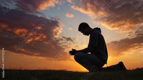 Wallpaper Mural A silhouette of a young man on his knees in prayer, clasping his hands under a vibrant sunrise sky, symbolizing sacrifice and devotion. Torontodigital.ca