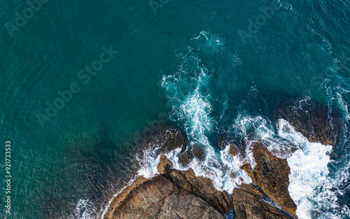 Fototapeta Naklejka Na Ścianę i Meble -  Aerial view of ocean waves crashing against rocks and creating a pattern of white foam.