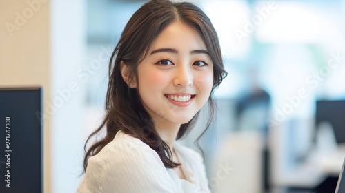 Free Download A young woman, smiling as she works on her laptop, is surrounded by a chic, minimalist home office interior in her beige shirt. - GFXLoad