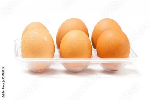 A row of light brown chicken eggs placed in a transparent holder, typically stored in the fridge. Photographed against a white background.