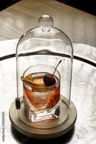Cocktail under a glass cover with a cherry on a black background