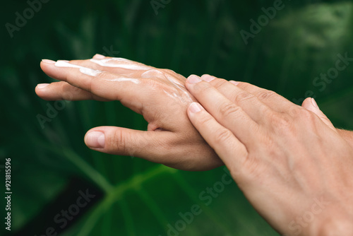 Close-up of Female Hands Applying Nourishing Cream, surrounded by tropical leaves