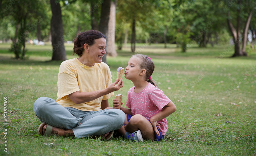 Happy family mom and child daughter eats ice cream having fun and doing picnic outdoor at city park on the green grass in summer day. Happy childhood. copy space Happy family mom and child daughter eats ice cream having fun and doing picnic outdoor at city park on the green grass in summer day. Happy childhood. copy space