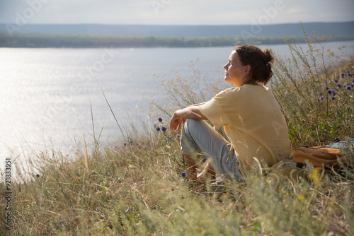 middle aged woman with a backpack  rests on the grass outdoor. copy space. Slow life. Enjoying the little things. spends time in nature in summer. Lykke concept