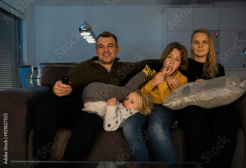 Fotografie A Caucasian family of four sitting on a couch in the living room watching televi
