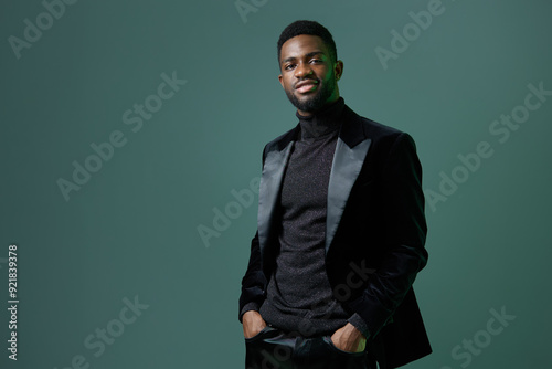 Confident man in black suit and turtleneck standing against green background in stylish and professional pose