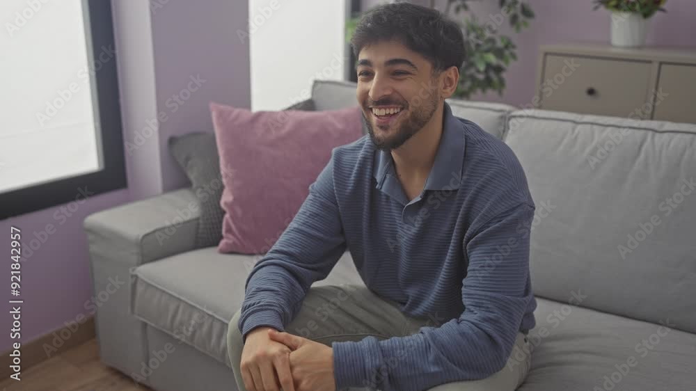 Handsome bearded man smiling in a modern living room setting, portraying a relaxed, casual atmosphere at home. Handsome bearded man smiling in a modern living room setting, portraying a relaxed, casual atmosphere at home.