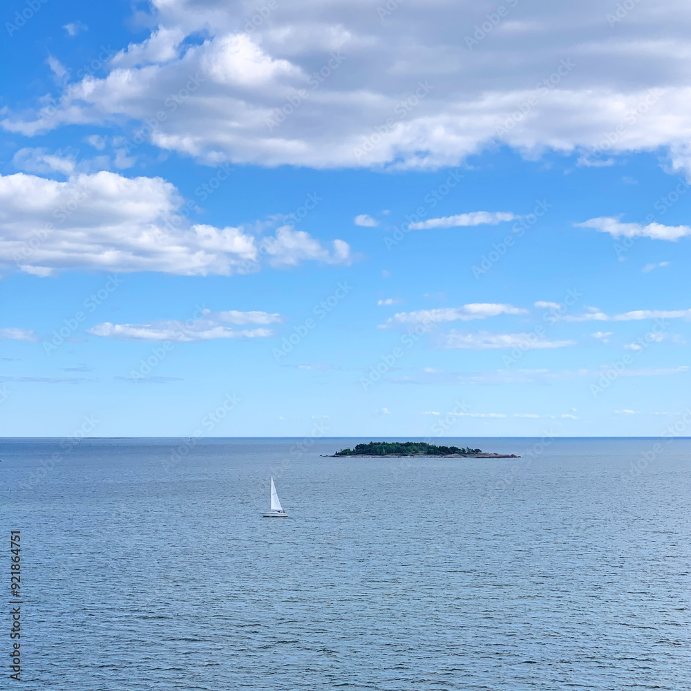 Fototapeta premium Yacht sailing along the island in the Baltic Sea with a blue sky and clouds near Vattuniemi, Helsinki, Uusimaa, Finland, August 2020