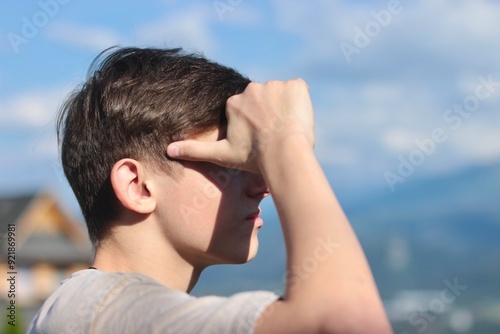 Portrait of a teenager who, covering himself from the sun's rays with his hands, looks at the big mountains.