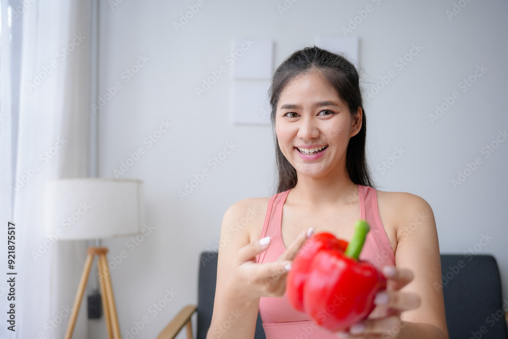 Young asian woman is smiling while holding a red bell pepper, promoting the benefits of a healthy lifestyle Young asian woman is smiling while holding a red bell pepper, promoting the benefits of a healthy lifestyle