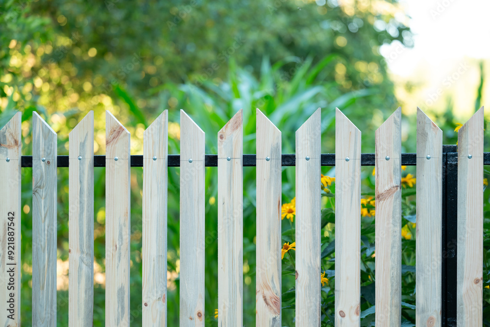 County style wooden fence with the garden on sunny summer day on background. Newly made fence in the countryside, renovation and improving of home plot by handiwork County style wooden fence with the garden on sunny summer day on background. Newly made fence in the countryside, renovation and improving of home plot by handiwork