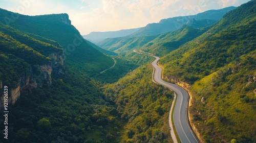 Aerial perspective of a road cutting through a scenic mountain pass with lush greenery and clear skies. Ideal for travel cont