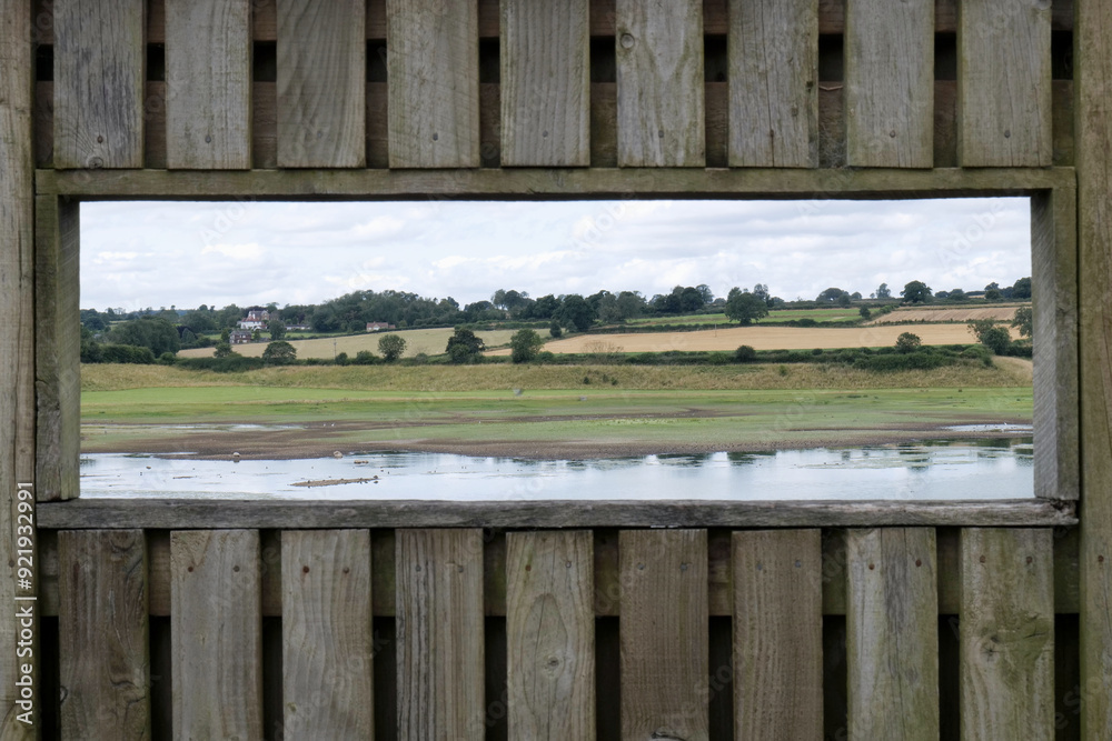 Outdoor bird hide window looking across onto wetlands and fields beyond in the summer time, with shallow depth of field. Outdoor bird hide window looking across onto wetlands and fields beyond in the summer time, with shallow depth of field.
