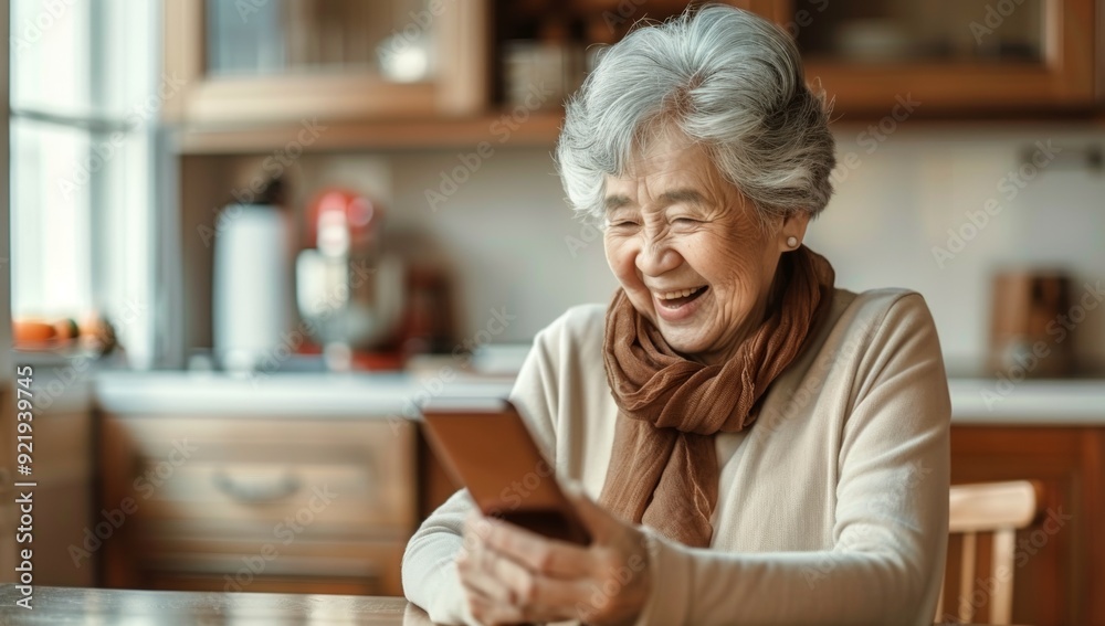 A woman is sitting in a kitchen and smiling while looking at her cell phone A woman is sitting in a kitchen and smiling while looking at her cell phone