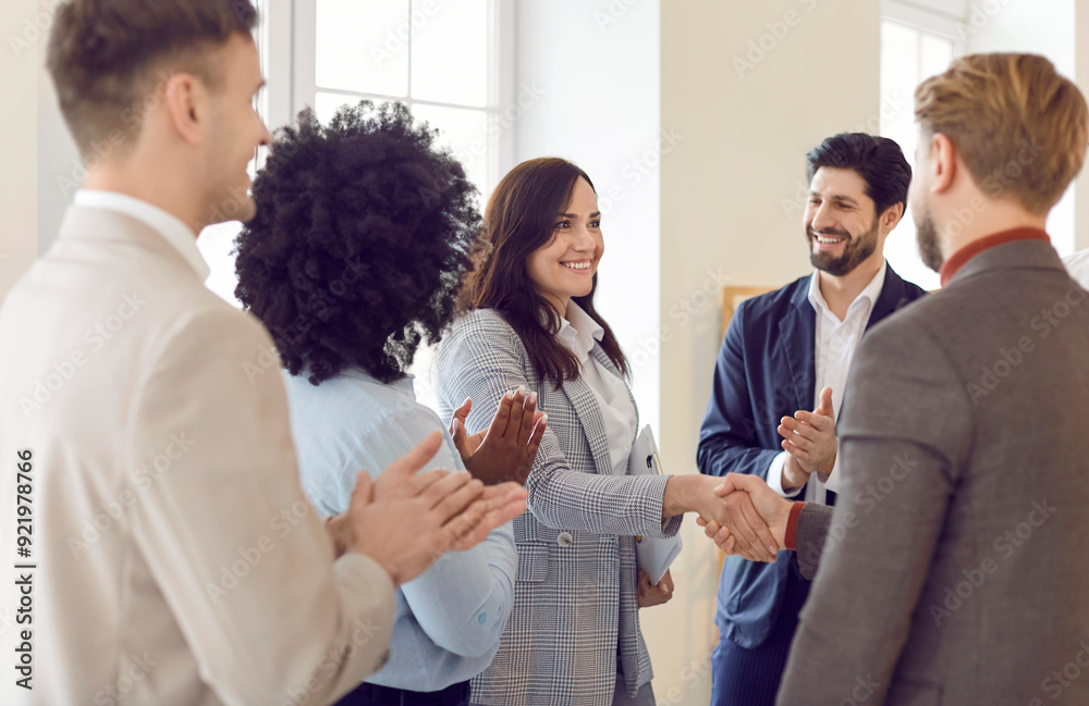 Woman shaking hands with a colleague during a meeting, surrounded by a team or group of applauding colleagues. People celebrating agreement or deal, successful and collaborative business environment. Woman shaking hands with a colleague during a meeting, surrounded by a team or group of applauding colleagues. People celebrating agreement or deal, successful and collaborative business environment.