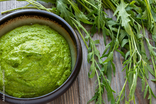 Wild arugula pesto with olive oil, sunflower seeds, and walnuts in a bowl. Wild arugula leaves on the side.  photo