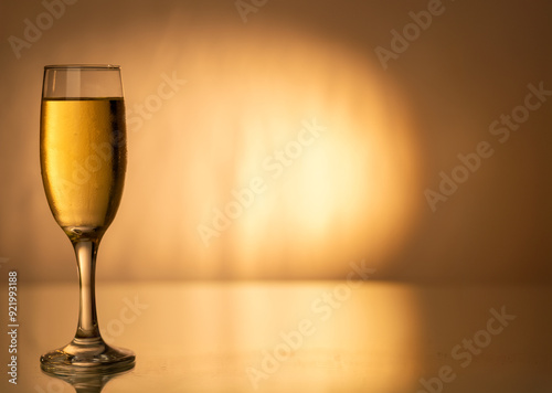 A champagne flute filled with cold champagne, placed on the left side of a gold gradient background, evoking the spirit of festive celebrations. photo