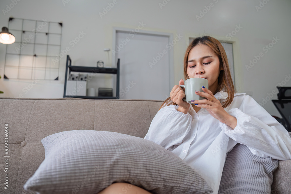 Young Woman Relaxing on Couch with Morning Coffee in Modern Home Interior Young Woman Relaxing on Couch with Morning Coffee in Modern Home Interior