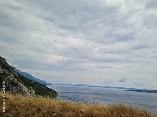 Scenic landscape of  mountains and sea on a cloudy summer day. People hurry up to vacation on of beautiful clean place by the Adriatic Sea. View of the coast of rocky island. Curve road in mountain.