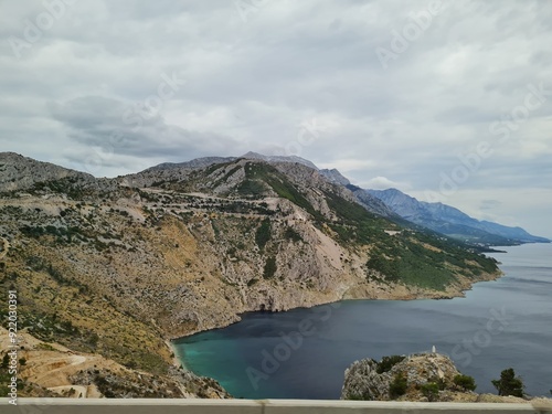 Scenic landscape of  mountains and sea on a cloudy summer day. People hurry up to vacation on of beautiful clean place by the Adriatic Sea. View of the coast of rocky island. Curve road in mountain.