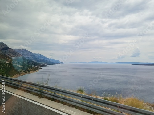 Scenic landscape of  mountains and sea on a cloudy summer day. People hurry up to vacation on of beautiful clean place by the Adriatic Sea. View of the coast of rocky island. Curve road in mountain.
