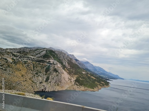 Scenic landscape of  mountains and sea on a cloudy summer day. People hurry up to vacation on of beautiful clean place by the Adriatic Sea. View of the coast of rocky island. Curve road in mountain.
