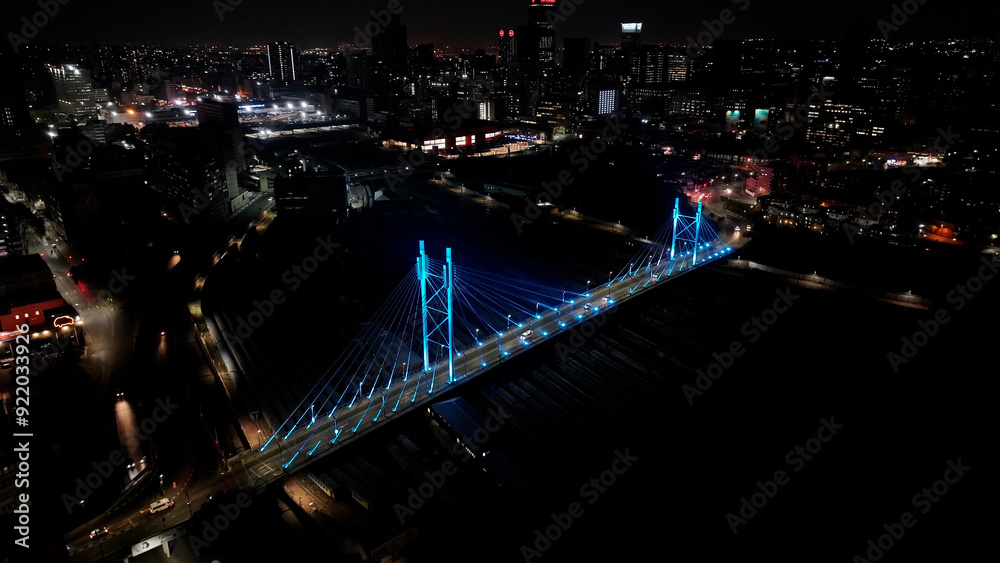 Naklejka premium Mandela Bridge At Johannesburg In Gauteng South Africa. Night Scape Town. Illuminated Cable Stayed Bridge. Johannesburg At Gauteng South Africa. Landmark Bridge. Colorful Skyline.