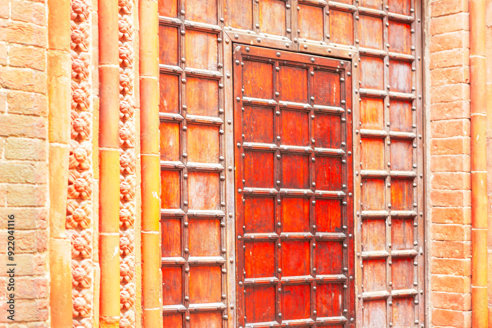 Large wooden door with a rich texture and natural grain. A wooden door with a metal frame and a brick wall behind it Large wooden door with a rich texture and natural grain. A wooden door with a metal frame and a brick wall behind it